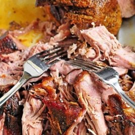 Pulled pork in a white baking dish with two forks.