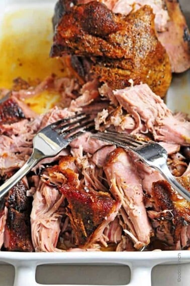 Pulled pork in a white baking dish with two forks.