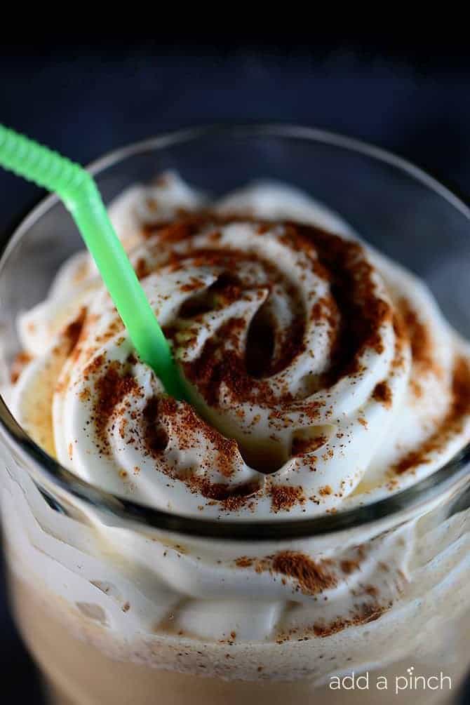 Closeup of Pumpkin Spice Latte topped with whipped cream and pumpkin spice in a clear glass with straw - addapinch.com