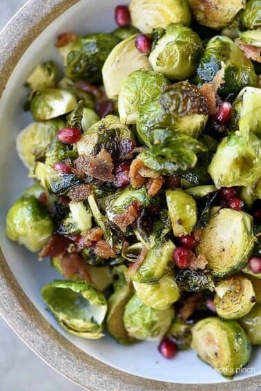 Roasted Brussels Sprouts with Pomegranate and Bacon Recipe - Roasted Brussels Sprouts with Pomegranate and Bacon make a delicious side dish! The brussels sprouts are roasted and then drizzled with maple syrup and balsamic vinegar and then tossed with crispy bacon and pomegranate! // addapinch.com