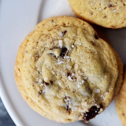 photograph of chocolate chip cookie on a white plate on a dark background.