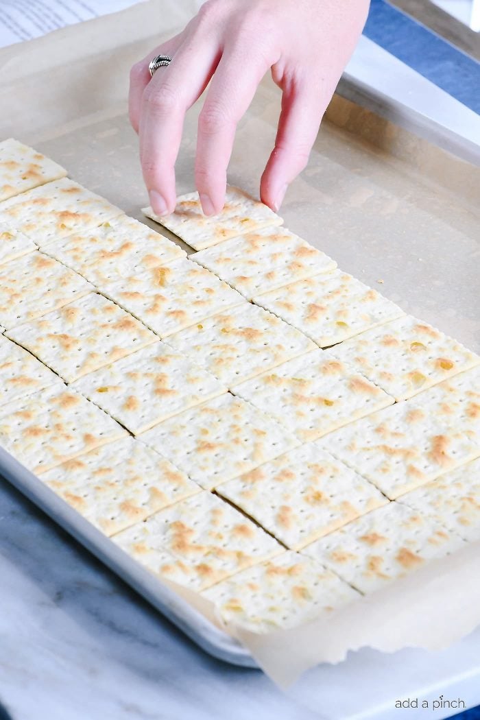 Laying saltine crackers on a baking sheet lined in parchment paper. 