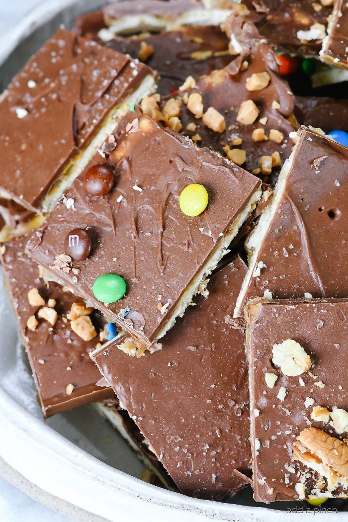 Cracker toffee is covered in chocolate, toffee bits, mini chocolate candies and nuts, all served on a tray.