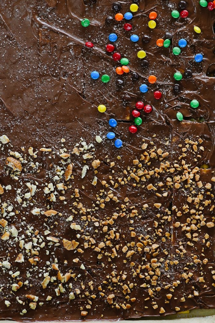 Baking sheet is full of chocolate covered cracker toffee sprinkled with nuts, toffee and mini chocolate candies. 