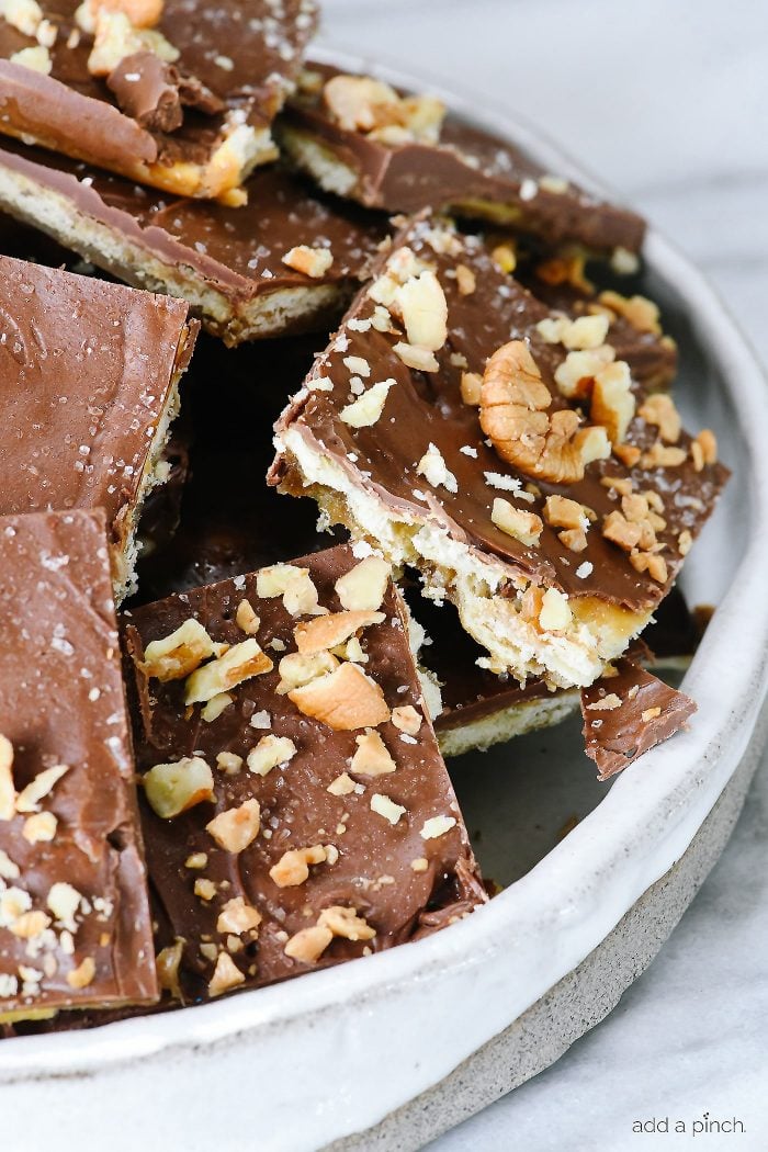 Stack of cracker toffee pieces topped with chocolate, salt and chopped nuts. 