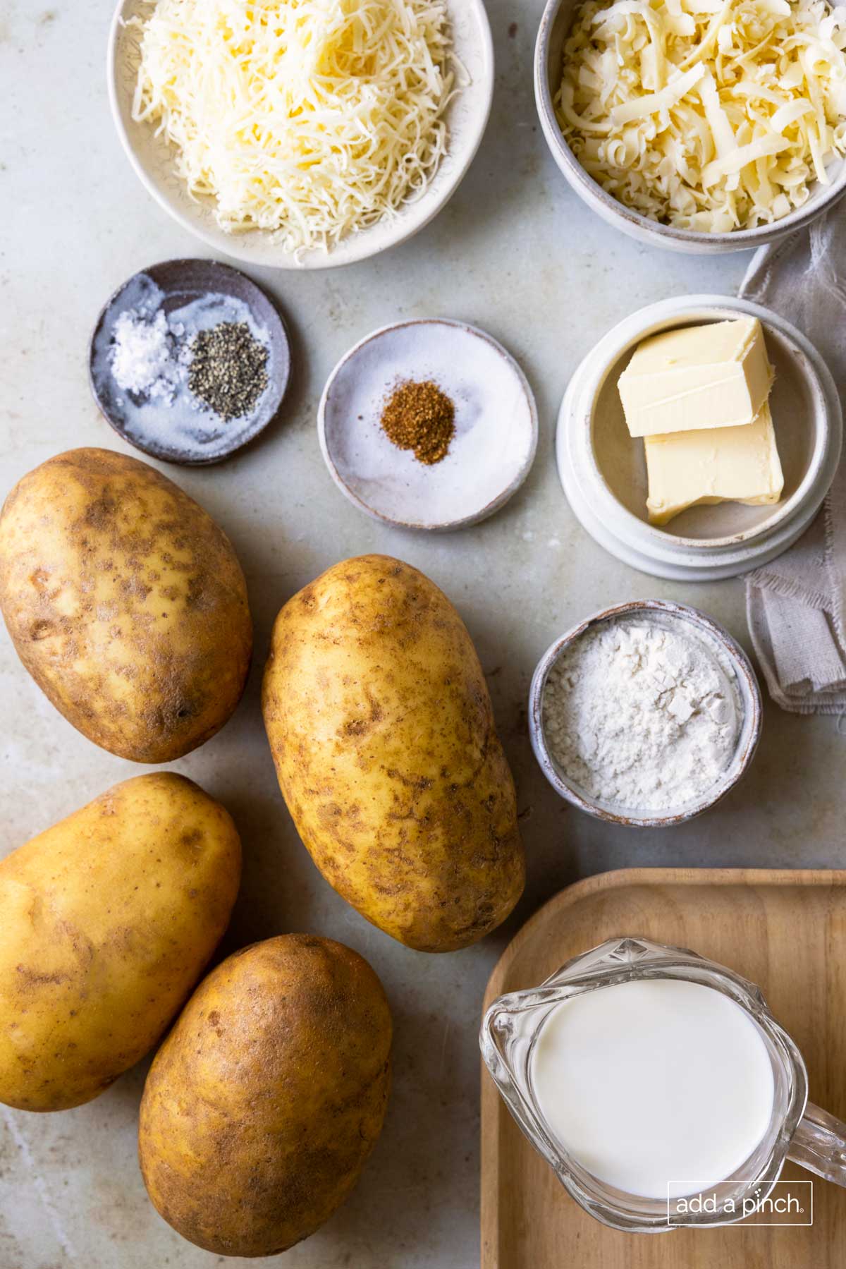 Potatoes, flour, butter, seasonings, milk and shredded cheese ready to be used to make a potato side dish.