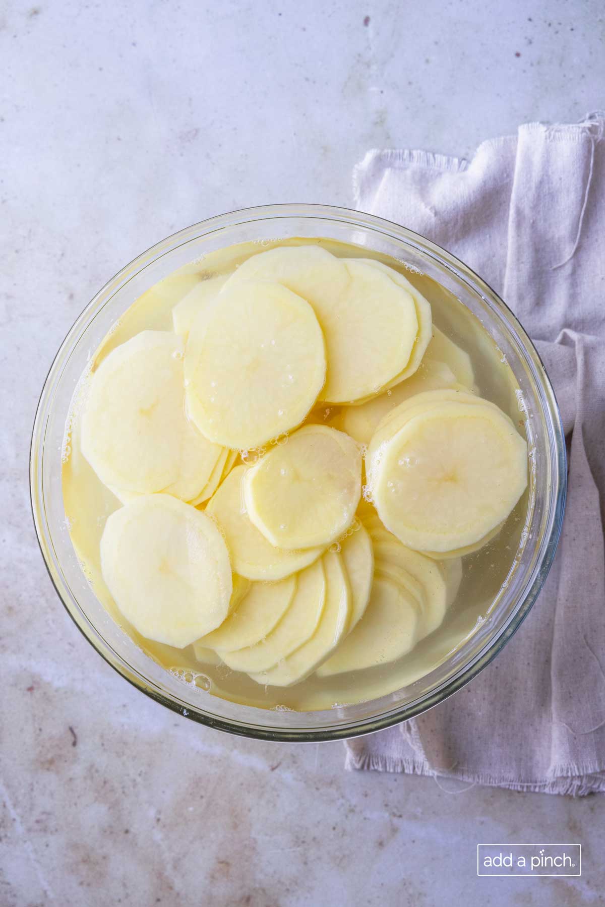 Sliced potatoes in a glass bowl filled with water.