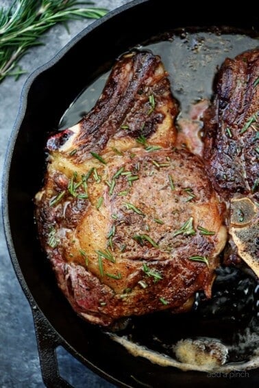 Cast iron skillet with a butter-basted ribeye steak topped with rosemary.