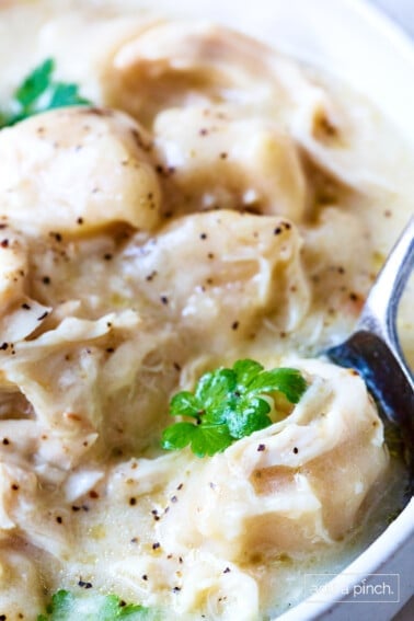 White soup bowl filled with crock pot chicken and dumplings with a bite on a spoon.