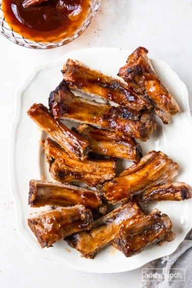 Photo of BBQ ribs on a white platter on a white background.