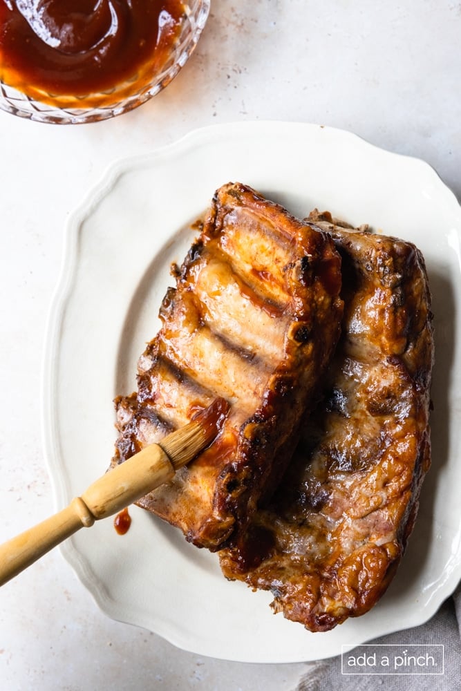 Ribs on a platter being brushed with additional BBQ sauce.