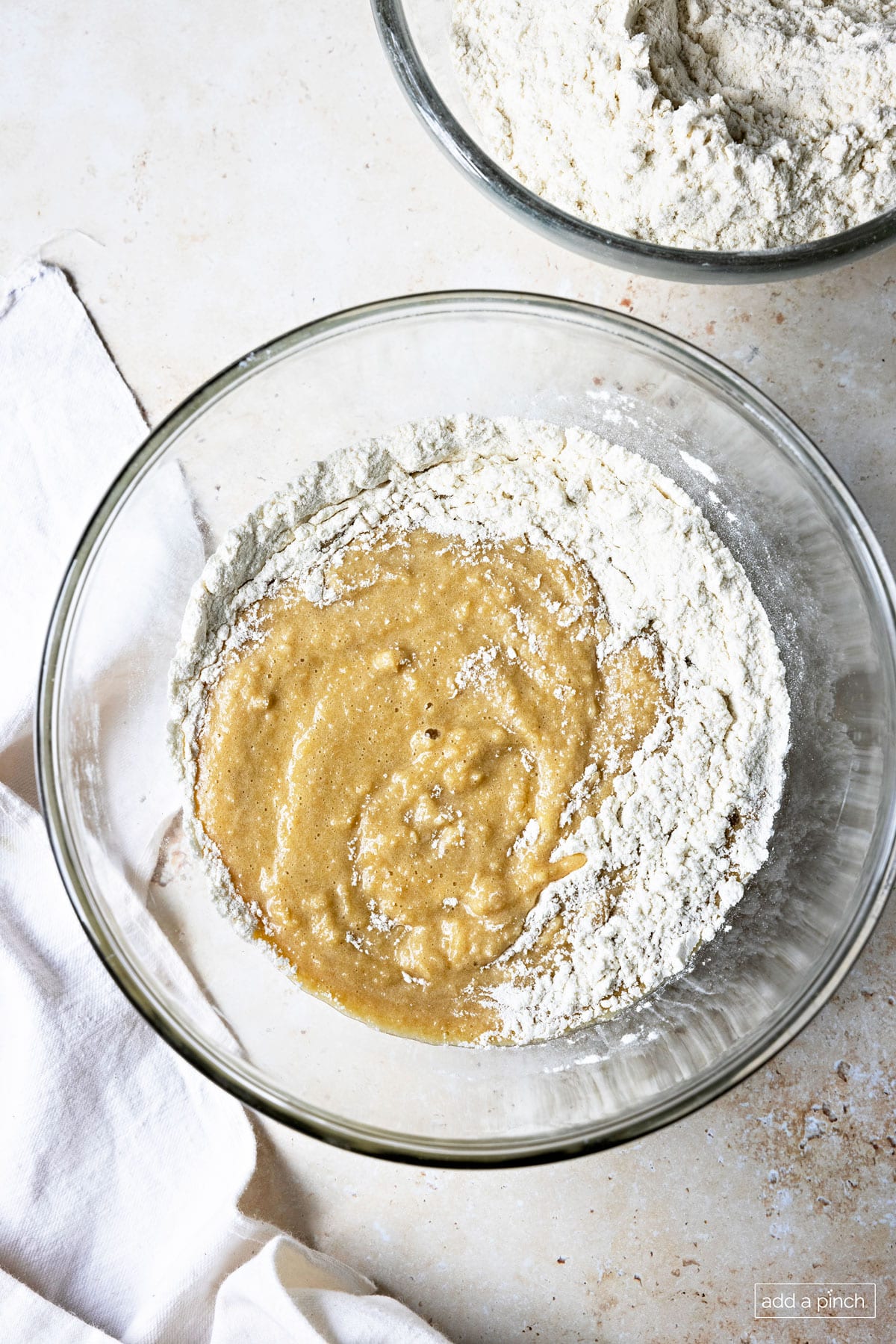 Photograph of wet ingredients being added to the dry ingredients in a glass bowl.