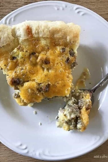 Photo of sausage cheddar quiche with pastry crust and fork with bite of quiche on white plate.