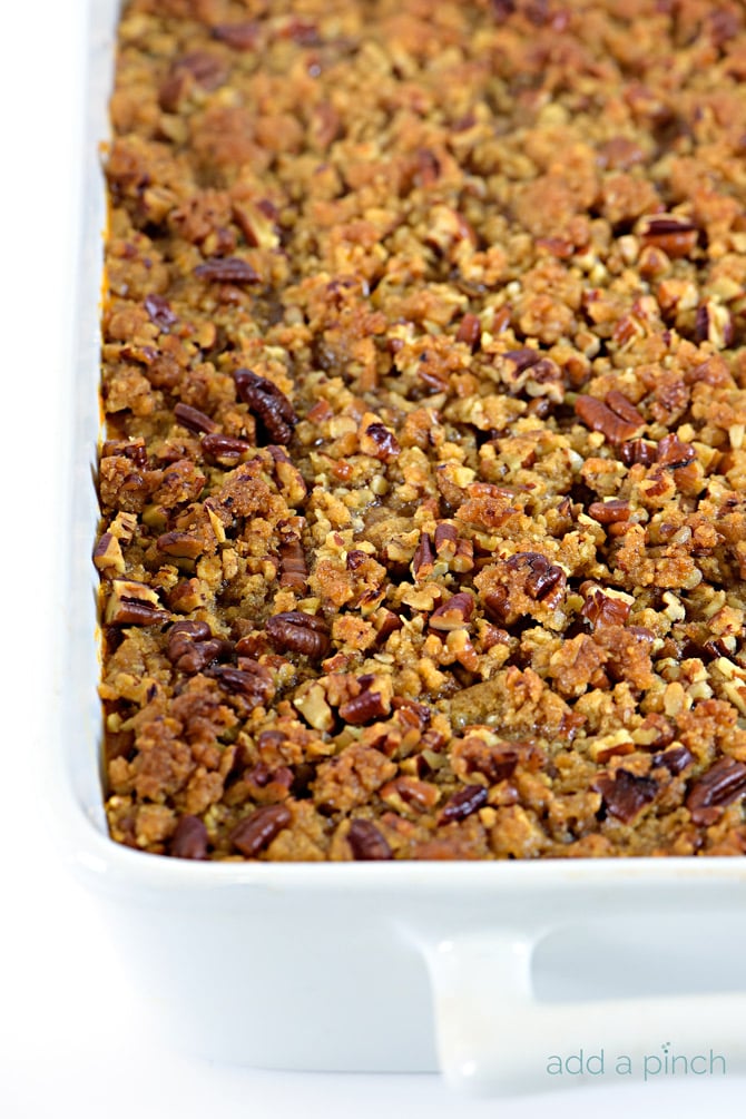 White casserole dish with handles holds Sweet Potato Casserole covered in nutty pecan crumble topping.