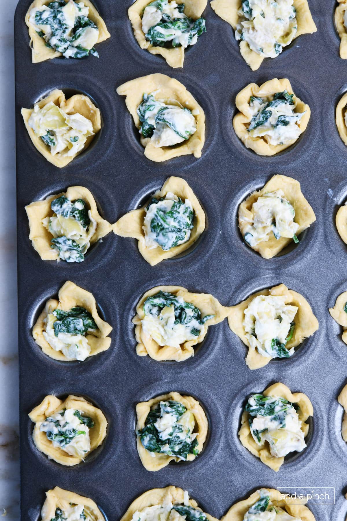 Muffin pan holds unbaked spinach dip bites that have been assembled prior to baking.