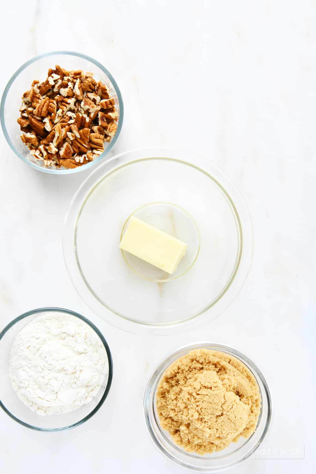 Glass bowls of brown sugar, flour, butter, and chopped pecans to make crumble topping.