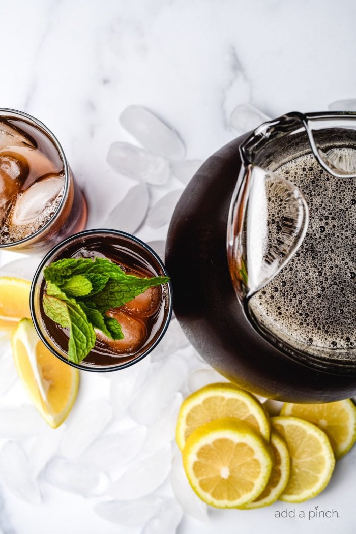 Overhead shot of gallon of sweet tea and two glasses with ice and min springs. Lemon slices and ice cubes are surrounding it.