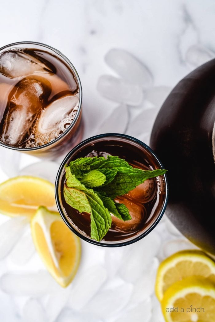 Iced Sweet tea in glasses garnished with mint sitting on ice cubes, surrounded by lemon slices.