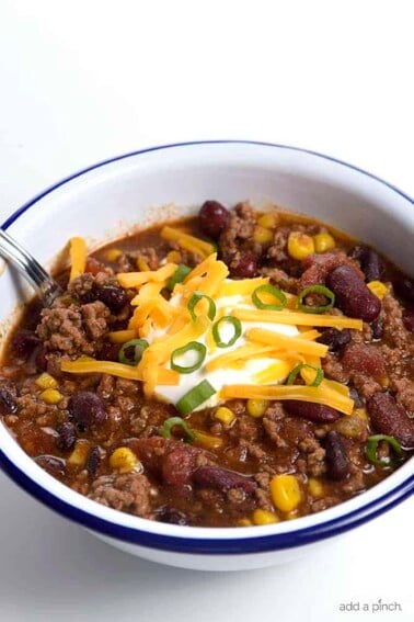 Taco Soup in a white bowl topped with sour cream, cheese, and green onions. #tacosoup #kidfriendly