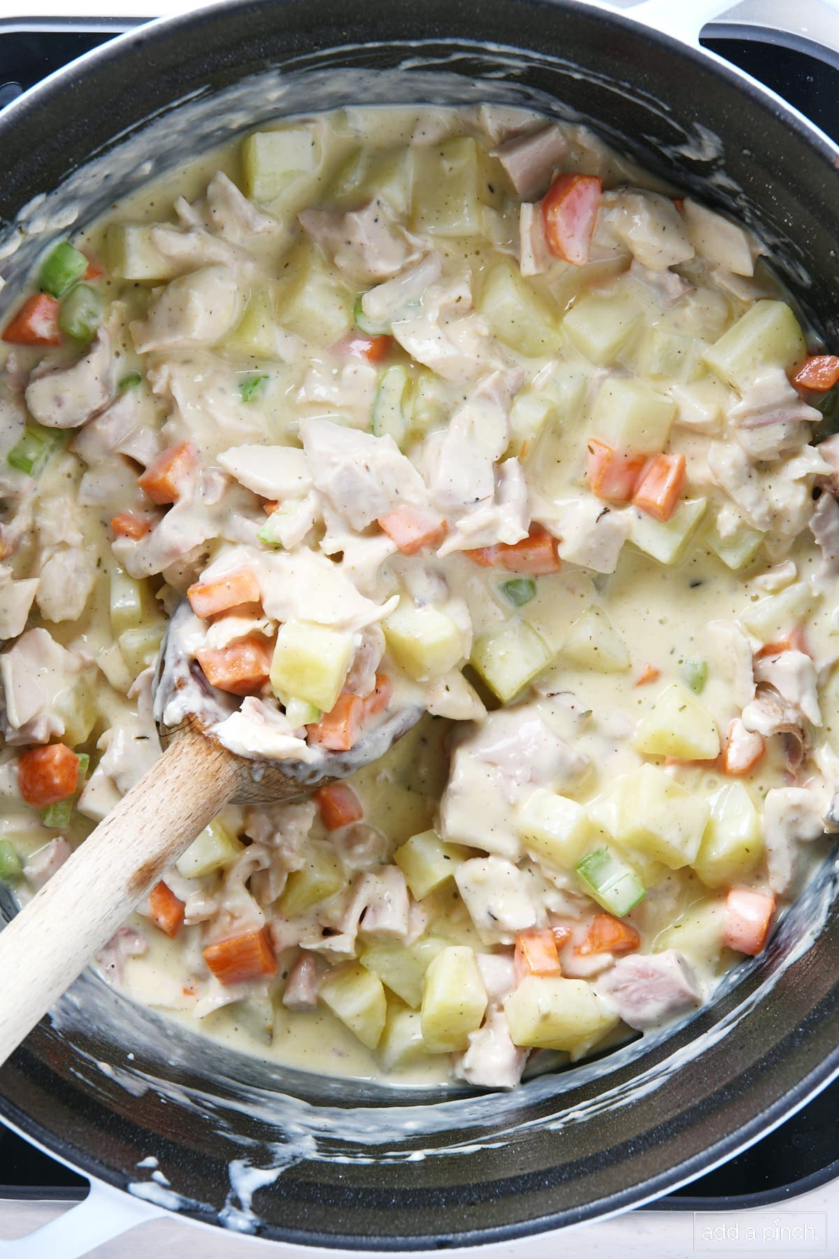 Cooked turkey pot pie filling in a Dutch oven with a wooden spoon.